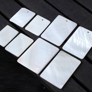 Puede incluir: Un conjunto de ocho azulejos rectangulares de nácar blanco con un agujero en la parte superior. Los azulejos están dispuestos en dos filas de cuatro, con el azulejo más grande en el centro.