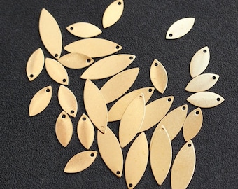 May include: A collection of gold-coloured metal leaf-shaped charms with a hole in the centre. The charms are scattered on a black surface.