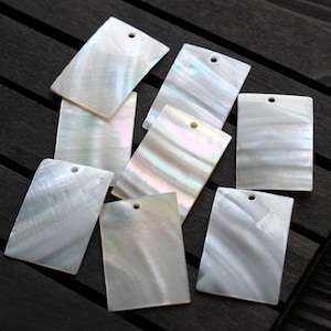 May include: Eight iridescent white rectangular mother of pearl shell pieces with a hole in the top for hanging.
