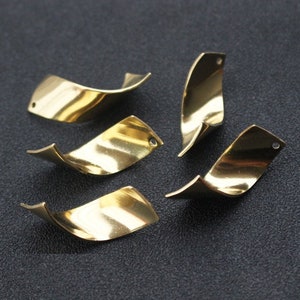 Könnte beinhalten: Fünf goldfarbene Metall-Anhänger mit einem gedrehten, wellenförmigen Design. Jeder Anhänger hat ein kleines Loch oben zum Anbringen an Schmuck oder andere Bastelarbeiten.