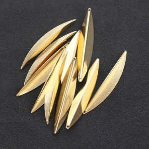 May include: A group of 10 gold-colored metal leaf-shaped charms. The charms are about 2 inches long and have a slightly curved shape.