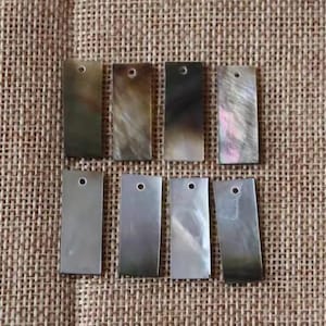 以下が含まれることがあります： 上部に穴が開けられた、黒色の真珠貝の矩形片が8つ。貝殻は自然な虹色の光沢を放っています。