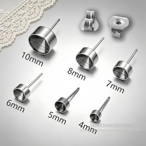 May include: A collection of silver-toned metal earring studs with circular settings in various sizes labelled 4mm, 5mm, 6mm, 7mm, 8mm, and 10mm. The set includes two metal earring backs. Each stud features a flat post and a hollow circular cup.