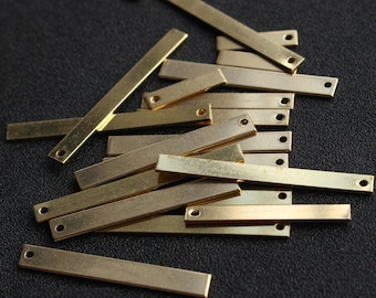 May include: A pile of gold-coloured metal bar pendants with two holes each. The bars are rectangular and have a slightly textured surface.