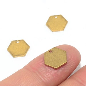 May include: Three gold-coloured metal hexagon charms with a small hole at the top for attaching to jewellery or other crafts.