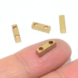 May include: Four gold-colored metal connector pieces with two holes each. The pieces are rectangular in shape and have a smooth, polished finish.