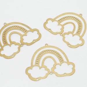 Könnte beinhalten: Drei goldene Regenbogen-Anhänger aus Metall mit Wolken. Jeder Anhänger hat ein ausgeschnittenes Design eines Regenbogens mit zwei Wolken.