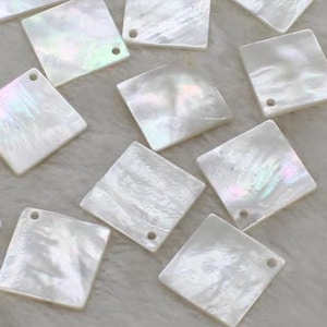 May include: A collection of white iridescent square-shaped shell pieces with a hole in the top for hanging.