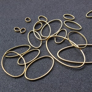Può includere: Una collezione di anelli ovali in metallo dorato di diverse dimensioni. Gli anelli sono disposti in modo casuale su una superficie grigio scuro.