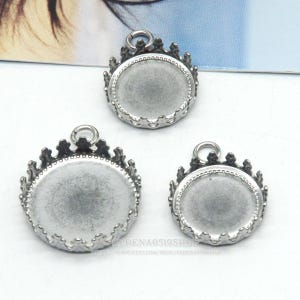 May include: Three silver-toned crown bezel pendant trays in varying sizes. Each tray has a circular recessed area for setting a cabochon or other embellishment. The crown design adds a decorative element to the pendants.