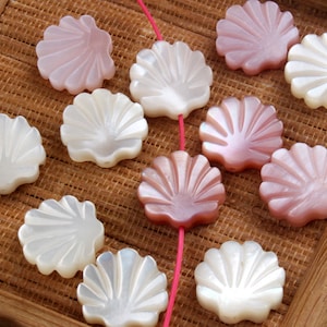 May include: A collection of white and pink shell-shaped beads with a textured surface. The beads are arranged on a woven surface.