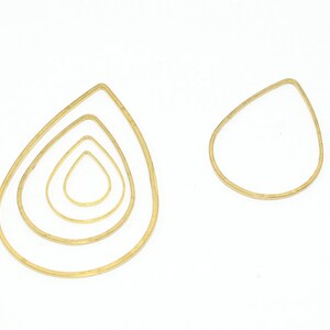 May include: Four gold teardrop-shaped wire hoops of varying sizes. The hoops are arranged in a nested pattern, with the largest hoop on the outside and the smallest hoop on the inside.
