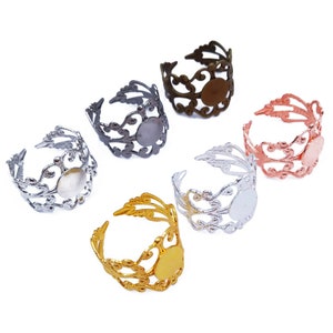 May include: Five adjustable ring blanks with filigree designs in silver, gold, and rose gold. Each blank has a round bezel for a cabochon.