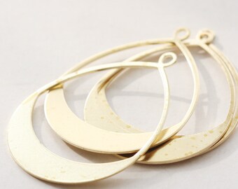 May include: Three gold-toned metal earring hoops with a teardrop shape. The hoops are layered on top of each other.