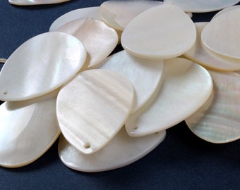 May include: A pile of white, pearlescent, oval-shaped shell pendants with a hole at the top for stringing.