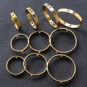 Puede incluir: Un conjunto de diez anillos de metal de color dorado con pequeños agujeros alrededor de los bordes. Los anillos son de diferentes tamaños y están dispuestos en un patrón aleatorio.