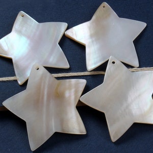 Puede incluir: Cuatro colgantes en forma de estrella blanca iridiscente con agujeros para colgar. Las estrellas están hechas de nácar y tienen una superficie ligeramente texturizada.