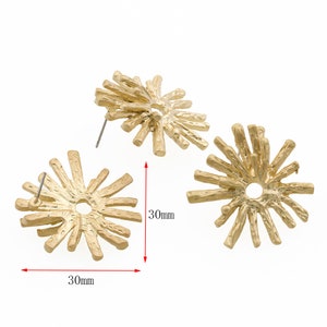 May include: Gold-colored, textured metal earrings in a starburst design. Each earring measures 30mm across. The earrings have a post backing for pierced ears. The design features radiating, textured lines emanating from a central hole.