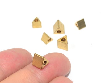 May include: Six gold-colored triangle-shaped metal beads with a hole in the center. The beads are scattered on a white surface, with one bead being held in a hand.