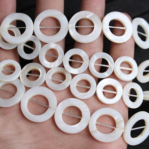 Może przedstawiać: Szereg białych pereł z masy perłowej z otworem w środku każdej perełki. Perły są nawleczone na biały sznurek.