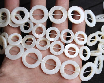 Peut inclure: Un brin de perles blanches en nacre avec un trou au centre de chaque perle. Les perles sont enfilées sur un cordon blanc.
