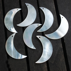 May include: Seven iridescent white mother of pearl crescent moon shapes with a hole at the top.