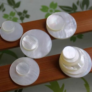 May include: A set of white mother-of-pearl round buttons in various sizes. The buttons are smooth and have a subtle iridescent sheen.