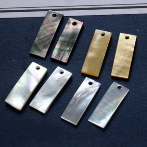 以下が含まれることがあります： 吊り下げ用の穴が上部に開いた、長方形の貝殻ペンダント8個の詰め合わせ。ペンダントは、黒、白、金、虹色など、さまざまな色があります。