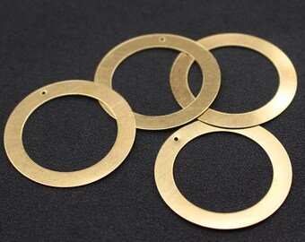 May include: Four gold-colored metal rings with a small hole at the top of each ring. The rings are arranged in a loose pile on a black surface.
