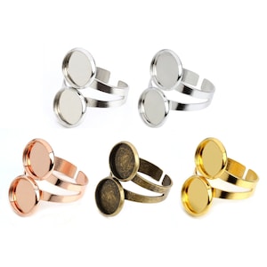 Op de afbeelding: Een assortiment verstelbare ringblanks in diverse metallic afwerkingen. De ringen hebben een dubbelbandontwerp met ronde bezel-instellingen, perfect voor het maken van aangepaste sieraden. Kleuren zijn zilver, roségoud, brons en goud.
