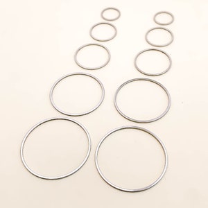 Könnte beinhalten: Ein Satz von zehn silberfarbenen Metallringen in verschiedenen Größen. Die Ringe sind in zwei Reihen zu fünf angeordnet, wobei der größte Ring unten und der kleinste Ring oben liegt.