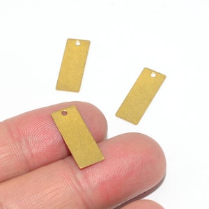 May include: Three gold-colored metal rectangular tags with a hole at the top. The tags are about 1 inch long and 1/2 inch wide.