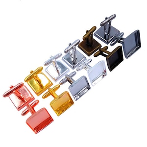 Puede incluir: Un surtido de gemelos cuadrados en varios acabados metálicos, incluyendo oro, plata, bronce y cobre. Los gemelos están dispuestos en diagonal, mostrando sus diferentes colores y diseños. Accesorios para vestimenta formal.