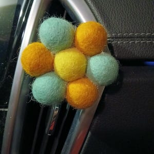 May include: A felt flower air freshener with six balls in a flower shape. The balls are in shades of yellow, orange, and green.