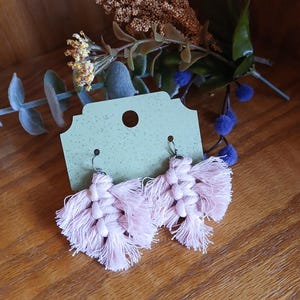 May include: A pair of pink tassel earrings with silver hooks. The earrings are hanging from a green card with a white circle in the center.