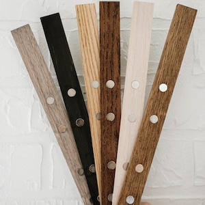 May include: Six long, narrow wooden strips arranged in a fan shape. Each strip features a distinct wood grain finish in shades of light gray, black, light oak, dark walnut, cream, and medium brown, with three circular silver magnets embedded.