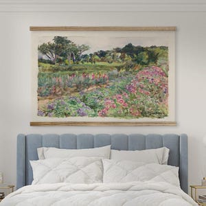Puede incluir: Una pintura de paisaje en acuarela que presenta un campo de flores coloridas en tonos rosas, morados y amarillos. La obra de arte está enmarcada con barras de madera y cuelga sobre una cama con cabecero azul y ropa de cama blanca.