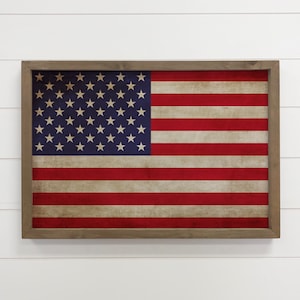 May include: A framed American flag with a distressed, vintage look. The flag is in a wooden frame with a brown finish.