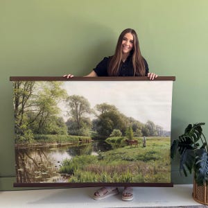 May include: A landscape painting depicting a serene river scene with trees, a horse, and a person. The artwork is mounted on a wooden frame. The color palette includes greens, browns, and blues, creating a tranquil atmosphere. The painting is a vintage style.