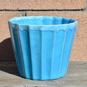 May include: A white ceramic mug with a black handle and the text "But First, Coffee" in a bold, black font. The mug is set against a blurred background, highlighting its clean design.