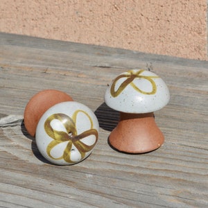 May include: Two ceramic mushroom salt and pepper shakers with brown and white speckled glaze. The tops of the shakers are white with a brown flower design.