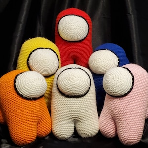 May include: Six crocheted plush toys shaped like the characters from the video game Among Us. The toys are in different colors, including red, yellow, orange, white, blue, and pink.