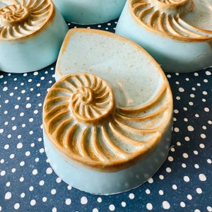 Può includere: Un set di quattro portasapone in ceramica blu e marrone a forma di conchiglia. I portasapone sono disposti su una superficie a pois neri e bianchi.
