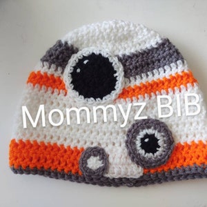 May include: White, orange, and gray crocheted hat with a black and white BB-8 design. The hat has the text "Mommyz BIB" on the front.