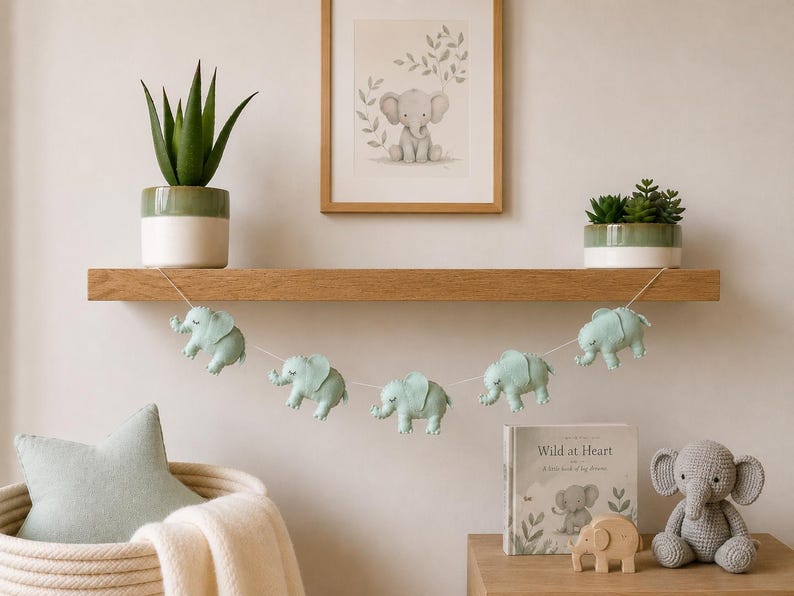 May include: A nursery shelf displays a garland of light blue elephant ornaments, a framed elephant print, and a stuffed elephant toy. A potted succulent and a book titled "Wild at Heart" are also visible.