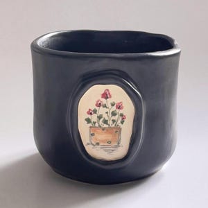 May include: A white ceramic mug with a black handle and the text "But First, Coffee" in a bold, black font. The mug is set against a neutral background, highlighting its simple design.