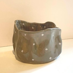 May include: A set of three ceramic mugs with a speckled, cream-colored glaze. Each mug features a different hand-painted design: a blue and green leaf, a yellow flower, and a red berry. The mugs have a simple, rounded shape.
