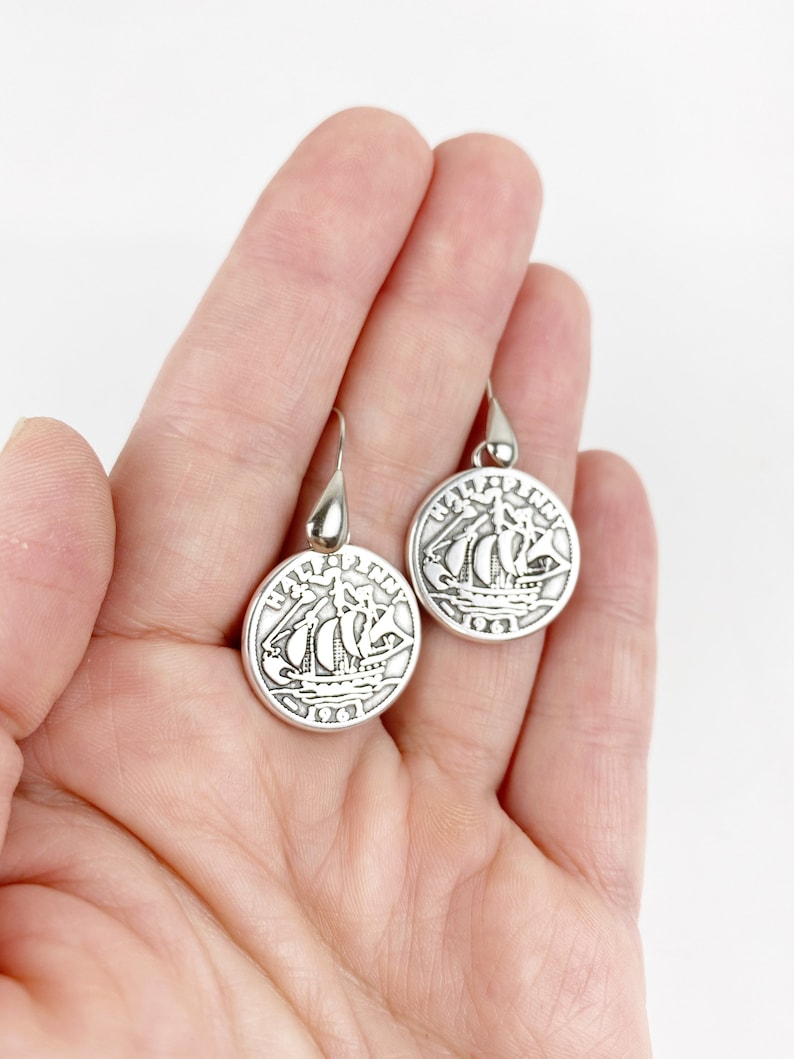 May include: A pair of silver dangle earrings featuring a vintage half penny coin with a ship design. The coin has the text "HALF PENNY" and "1961" on it.