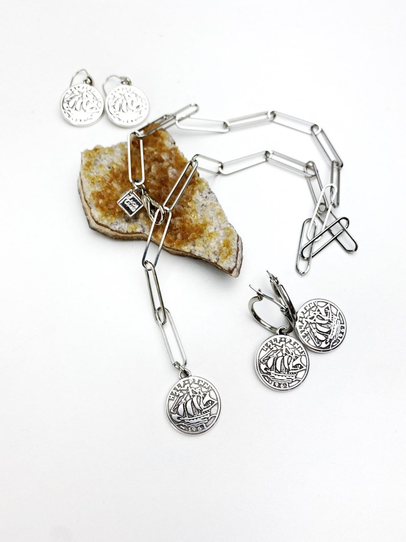 May include: A silver necklace with a silver charm of a ship and a silver chain. The necklace is on a piece of yellow rock. There are also two silver earrings with ship charms.