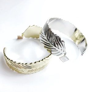 May include: Two gold and silver leaf-shaped bangle bracelets. The silver bracelet has a small tag with the word "Feather" on it.